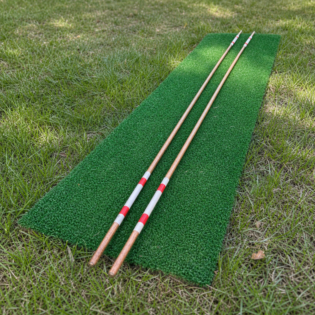 Two hand-painted hickory golf alignment sticks laid parallel on a green practice mat.