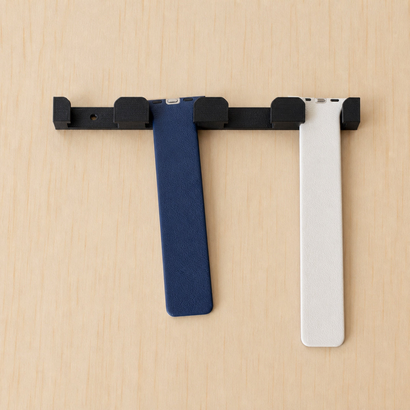 A black four-band wall holder on light wood with blue and white Apple Watch bands hanging from it.