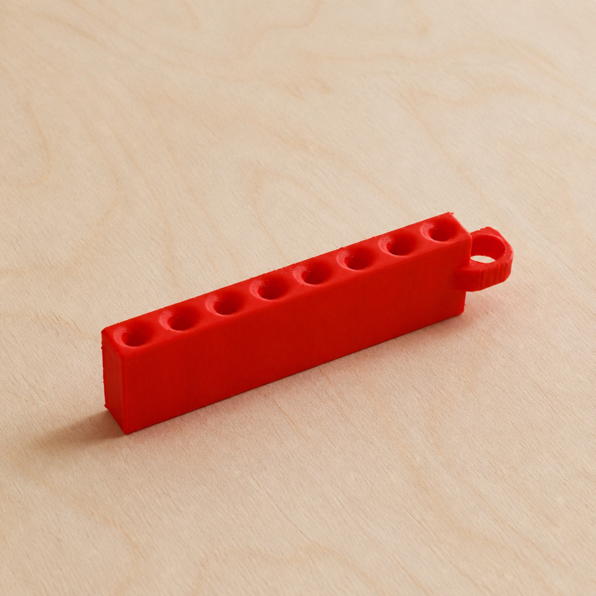 Red Golf Tee Holder with eight tee openings and hanging loop on pale wood