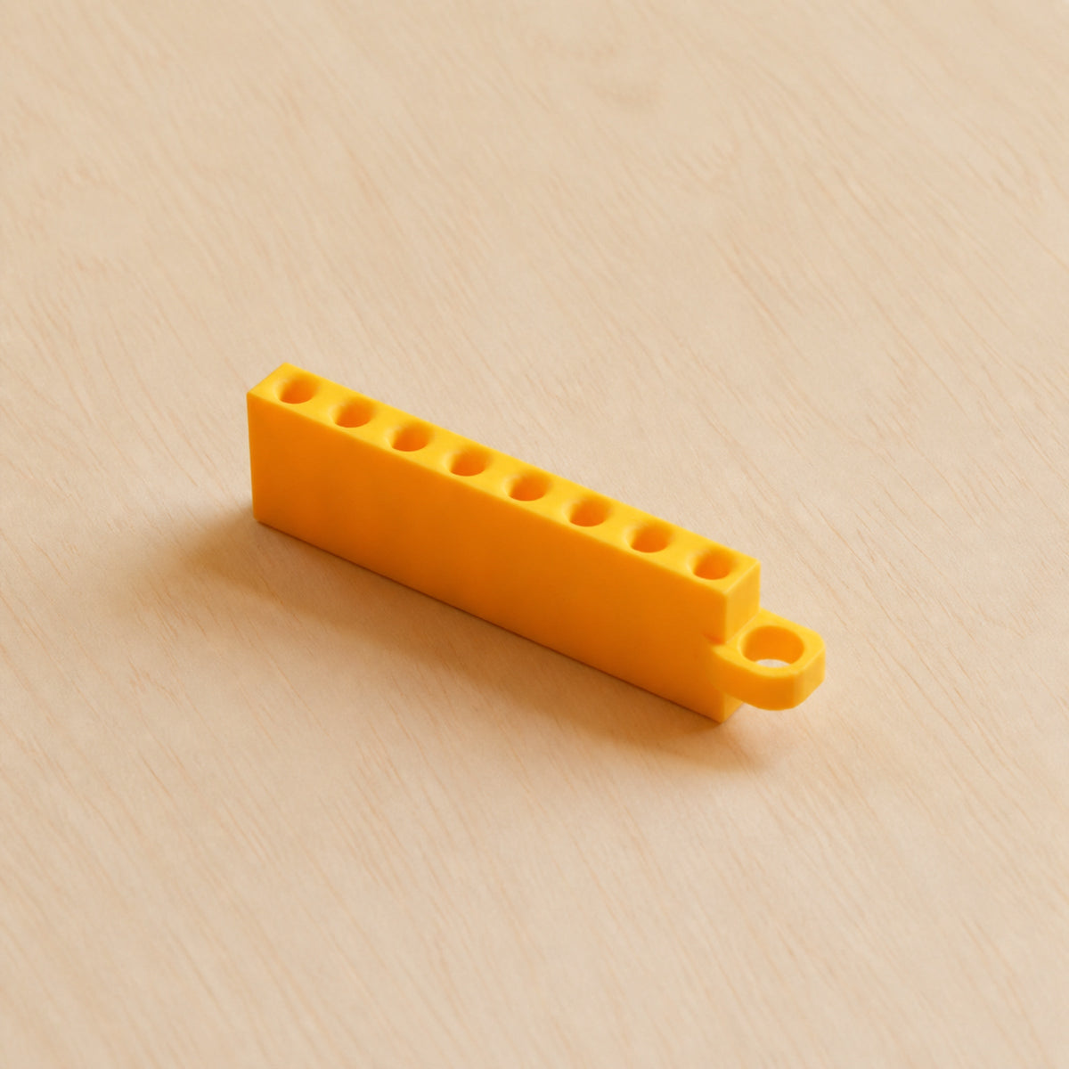 Yellow Golf Tee Holder with eight tee openings and hanging loop on pale wood