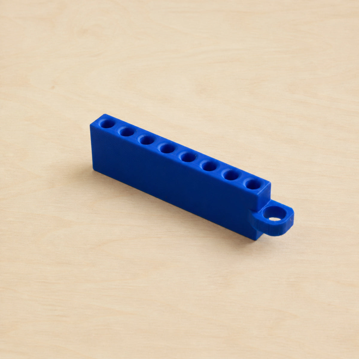 Blue Golf Tee Holder with eight tee openings and hanging loop on pale wood