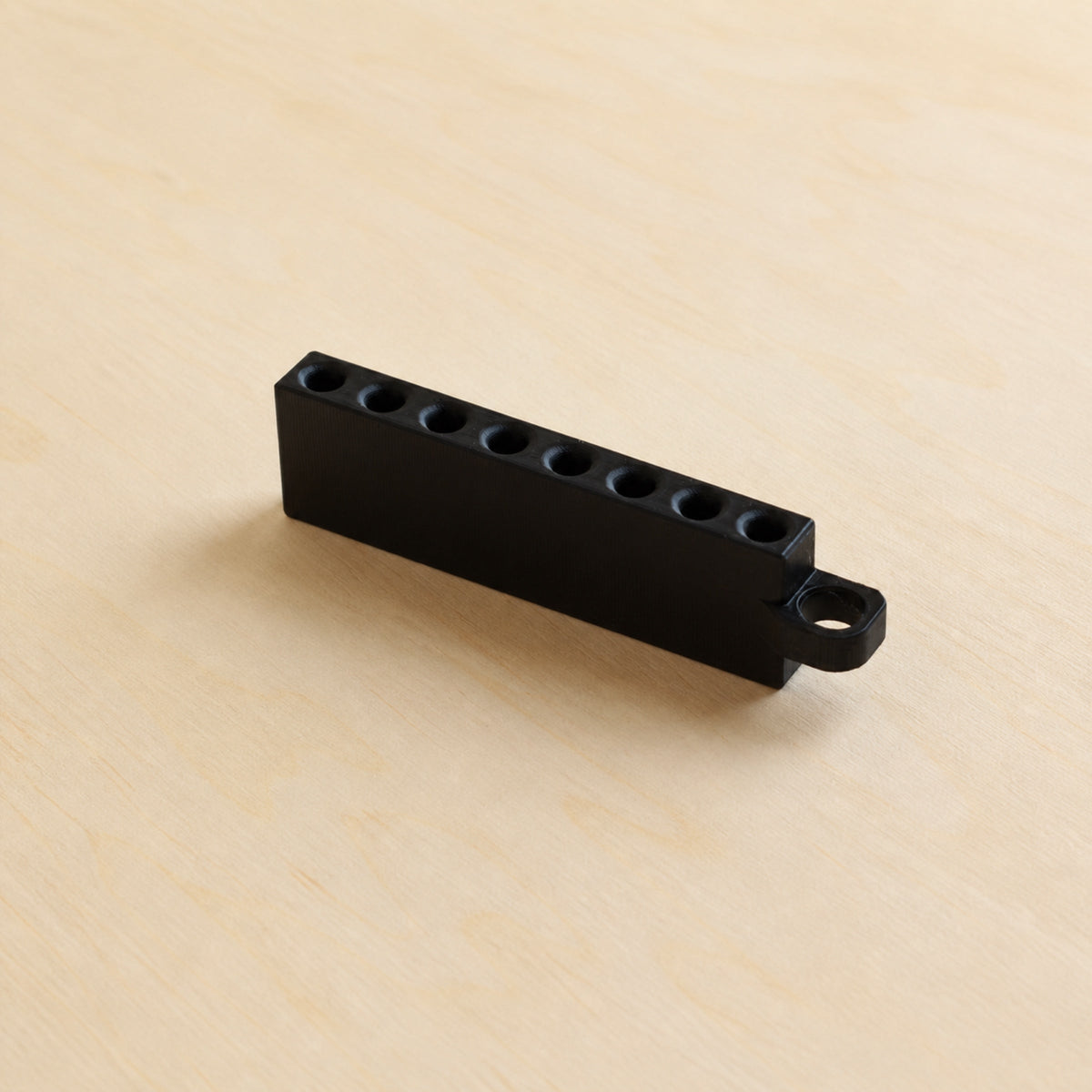 Black Golf Tee Holder with eight tee openings and hanging loop on pale wood