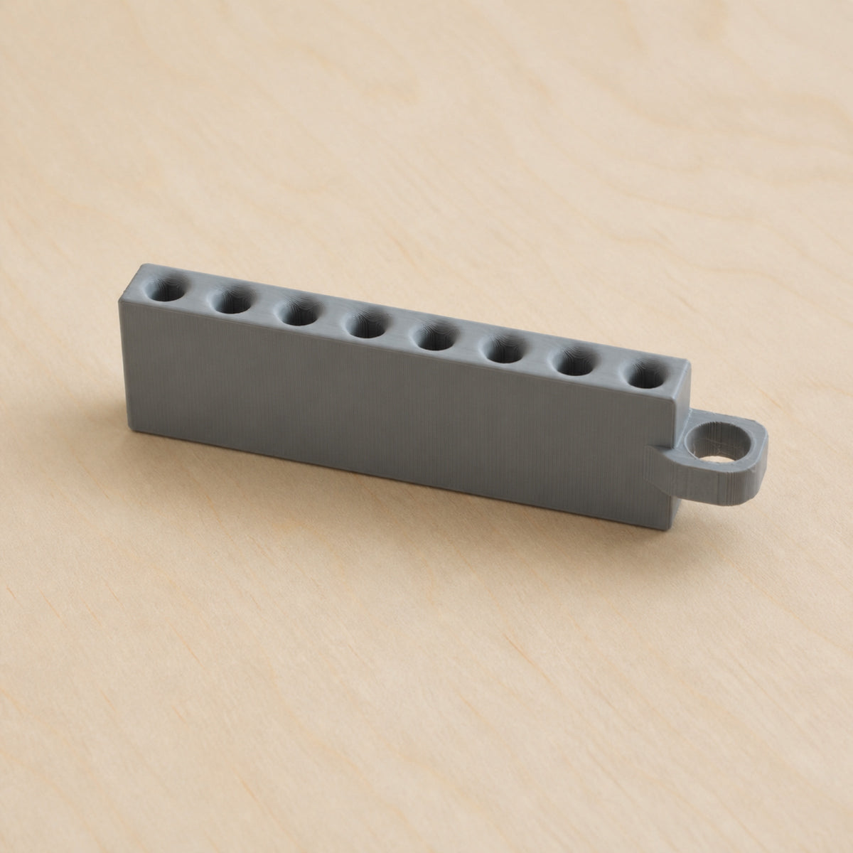 Grey Golf Tee Holder with eight tee openings and hanging loop on pale wood