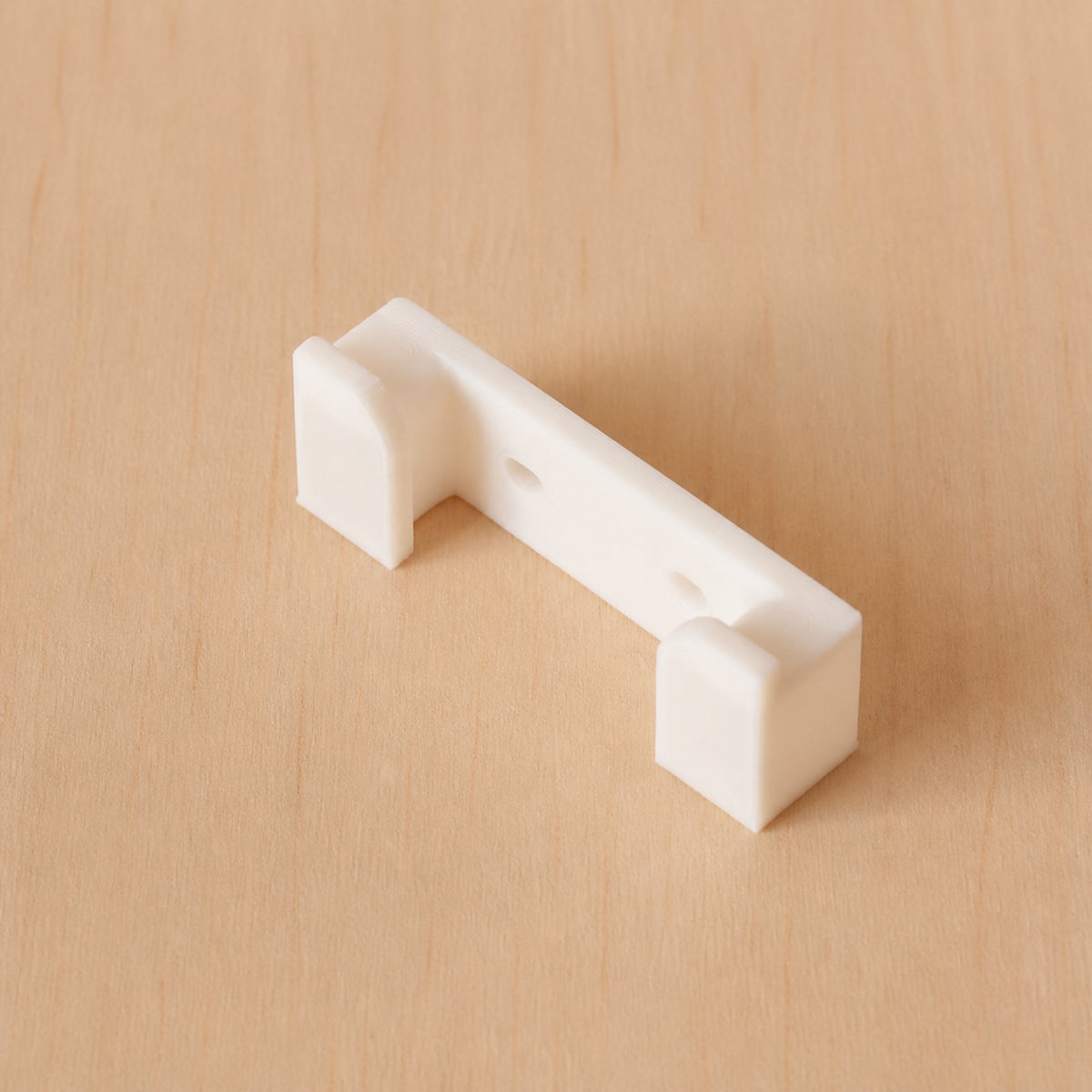 White one-band Apple Watch band wall holder shown at an angle on warm plywood