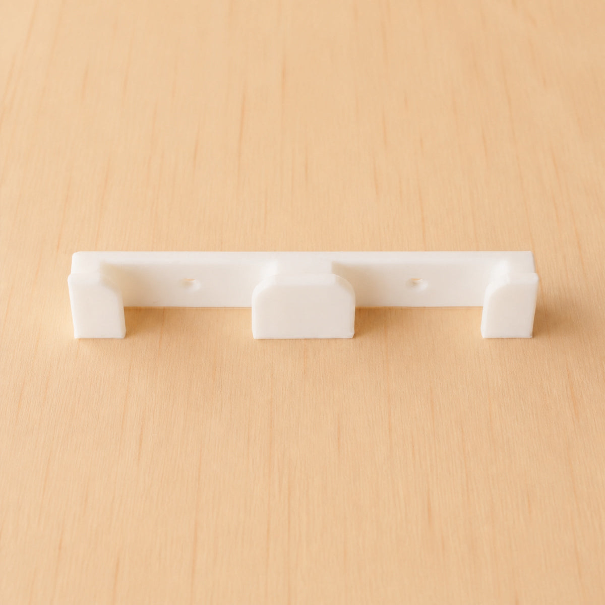White two-band Apple Watch band wall holder shown from the front on warm plywood