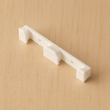 White two-band Apple Watch band wall holder shown at an angle on warm plywood