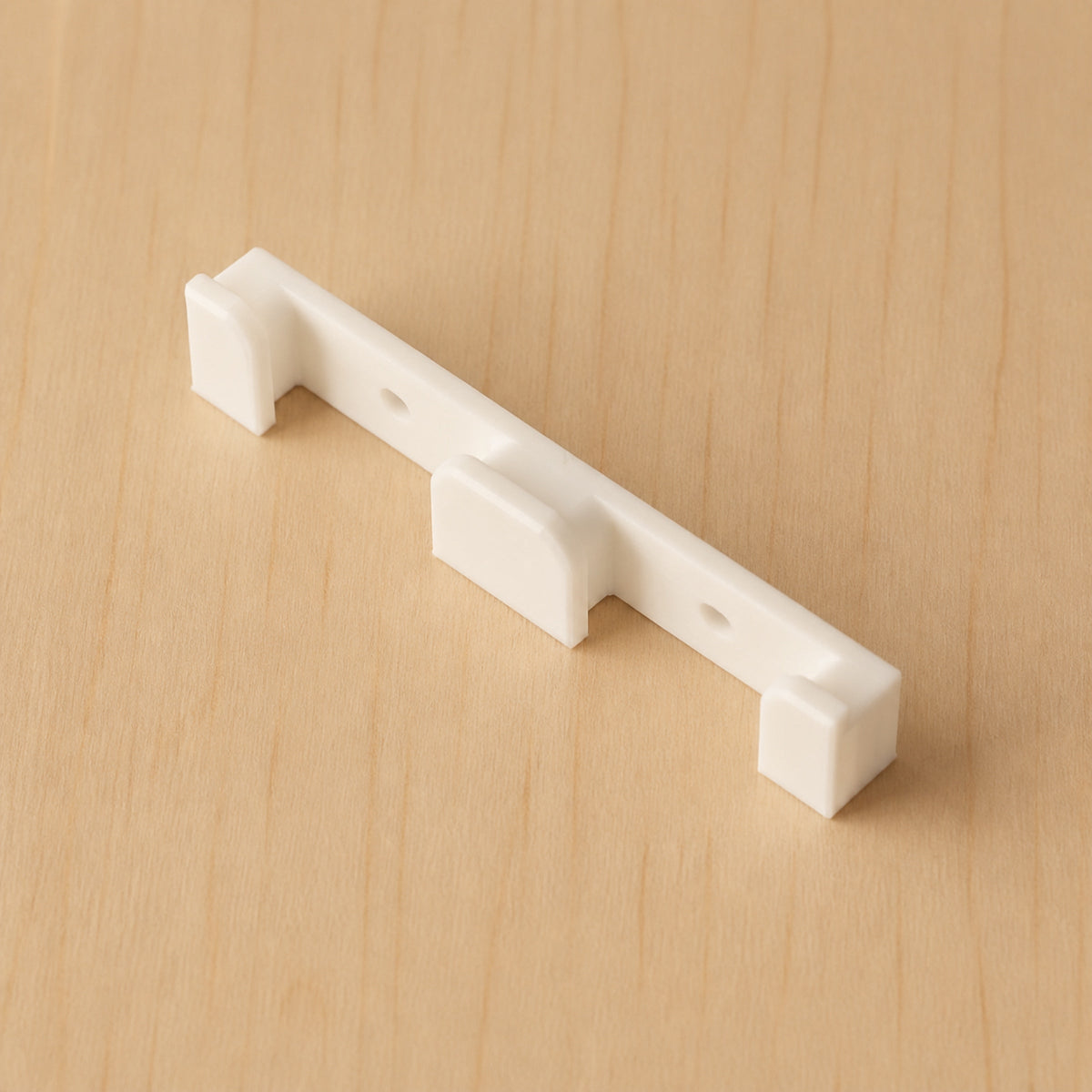 White two-band Apple Watch band wall holder shown at an angle on warm plywood