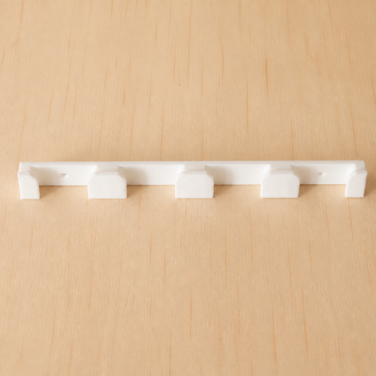 White four-band Apple Watch band wall holder shown from the front on warm plywood