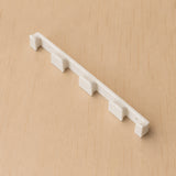 White four-band Apple Watch band wall holder shown at a wide angle on warm plywood