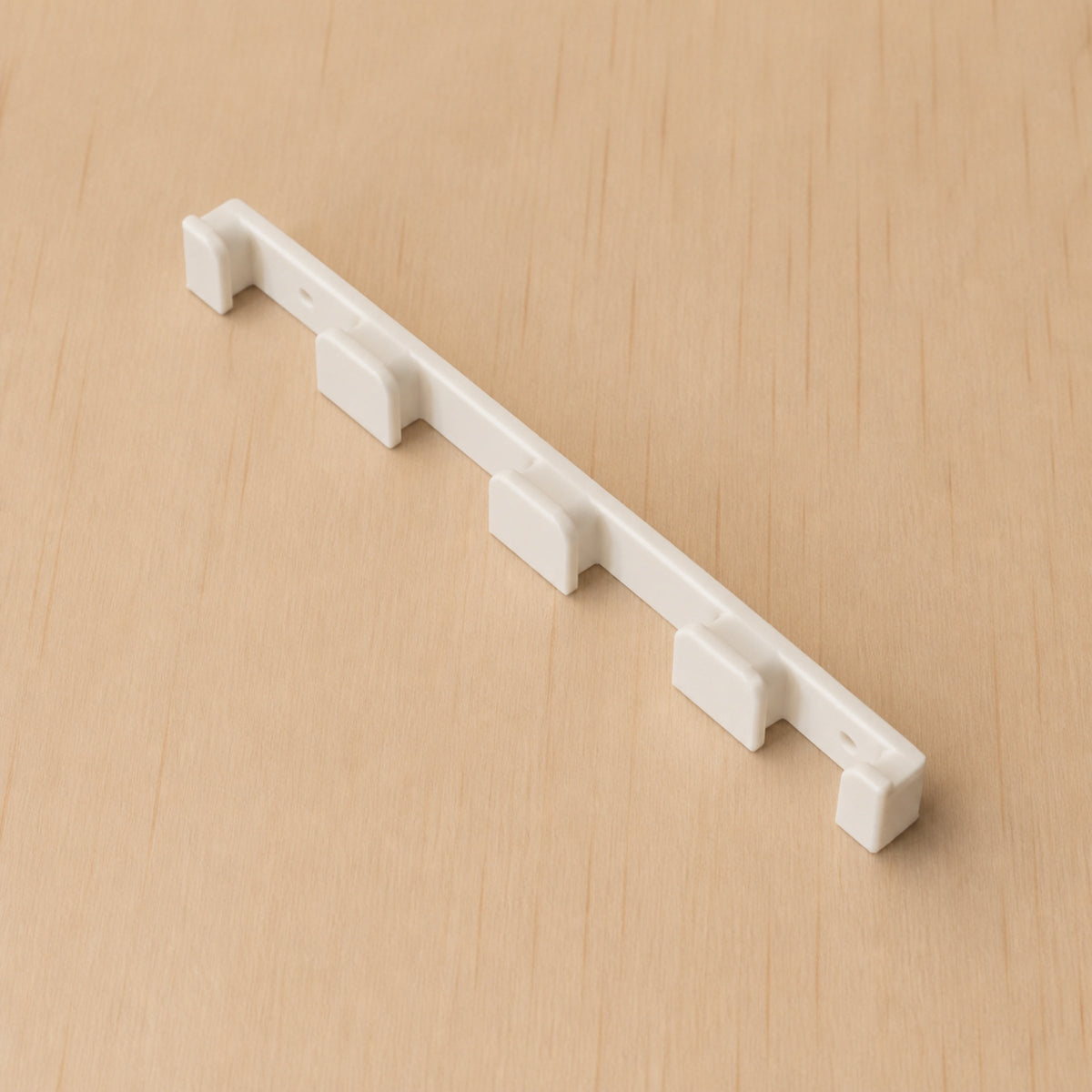 White four-band Apple Watch band wall holder shown at a wide angle on warm plywood