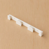 Close angled view of a white four-band Apple Watch band wall holder on warm plywood