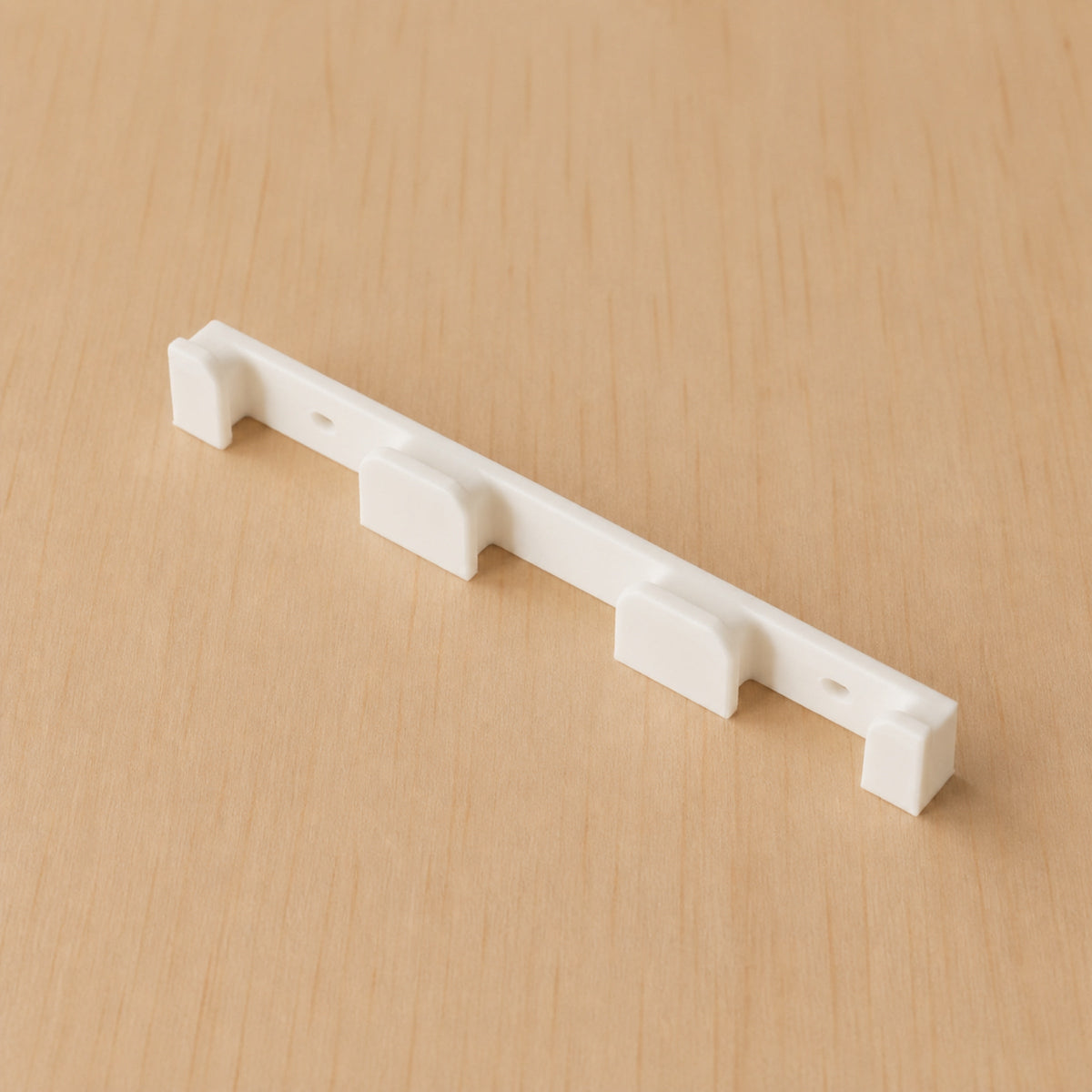 Close angled view of a white four-band Apple Watch band wall holder on warm plywood