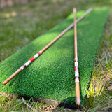 Two handmade hickory golf alignment sticks crossed on a practice mat