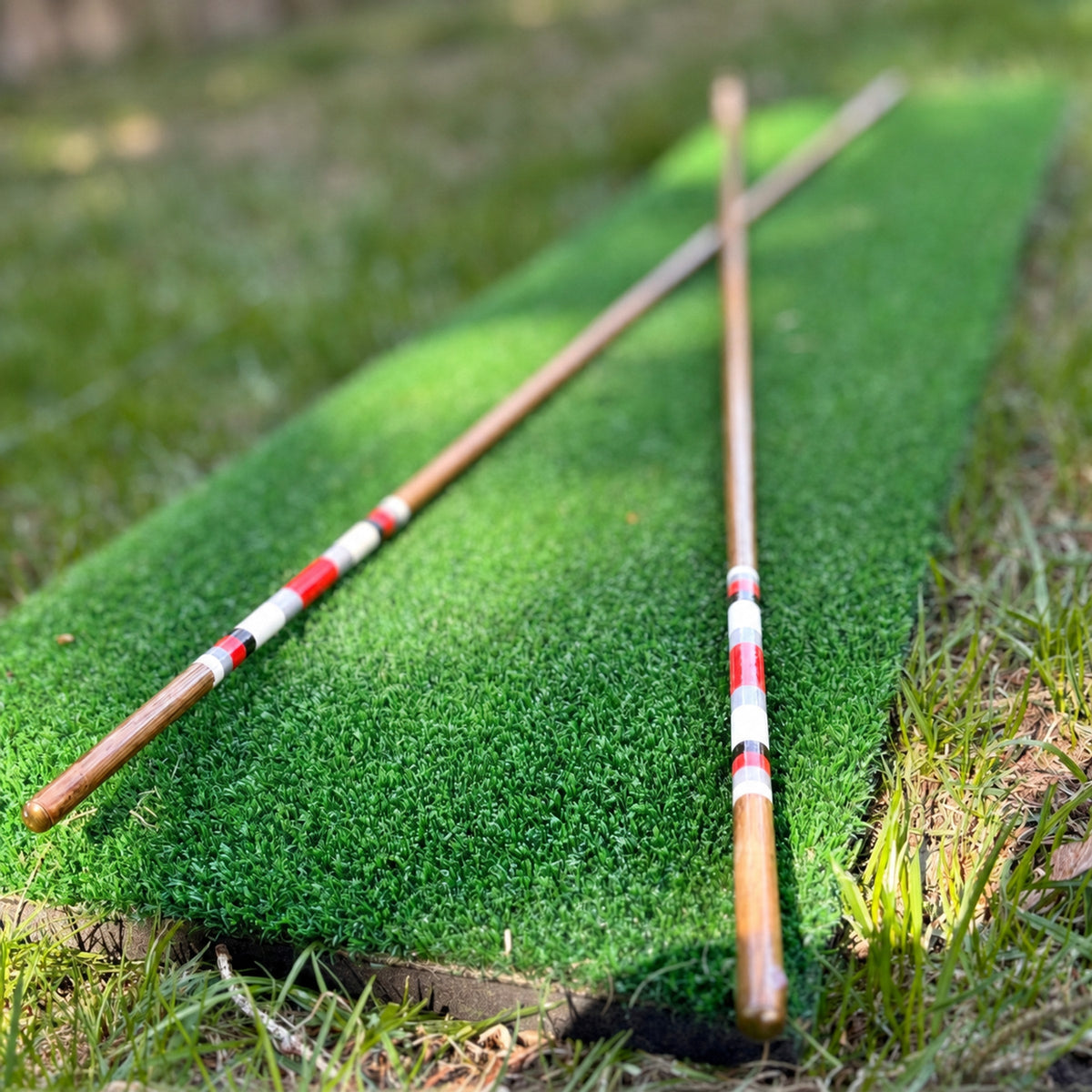 Two handmade hickory golf alignment sticks crossed on a practice mat