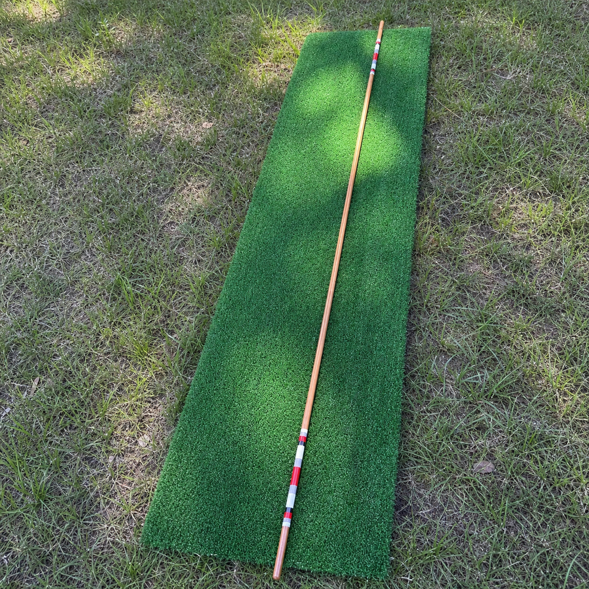 Full length handmade hickory golf alignment stick on a practice mat