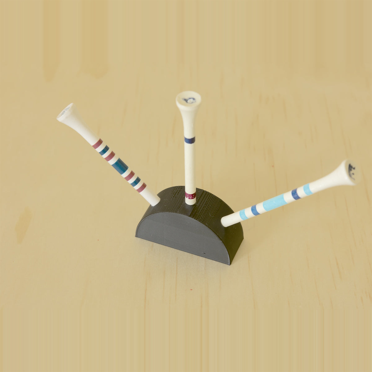 Black curved golf tee display holding three tees on a pale wood surface