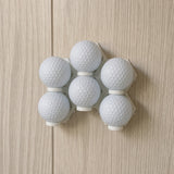 Six plain white golf balls arranged in installed modular wall display mounts
