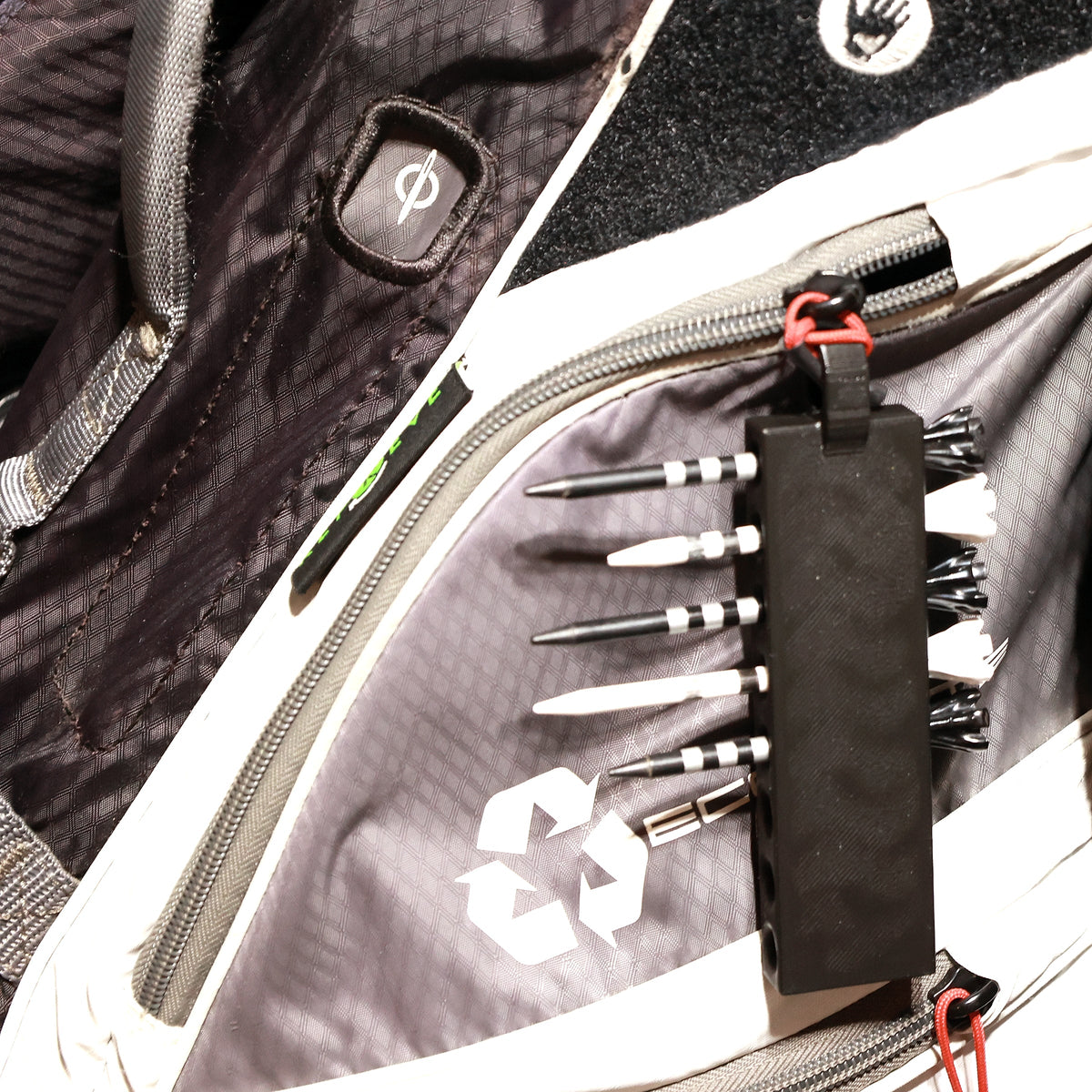 Black golf tee holder loaded with eight tees and hanging from a golf bag