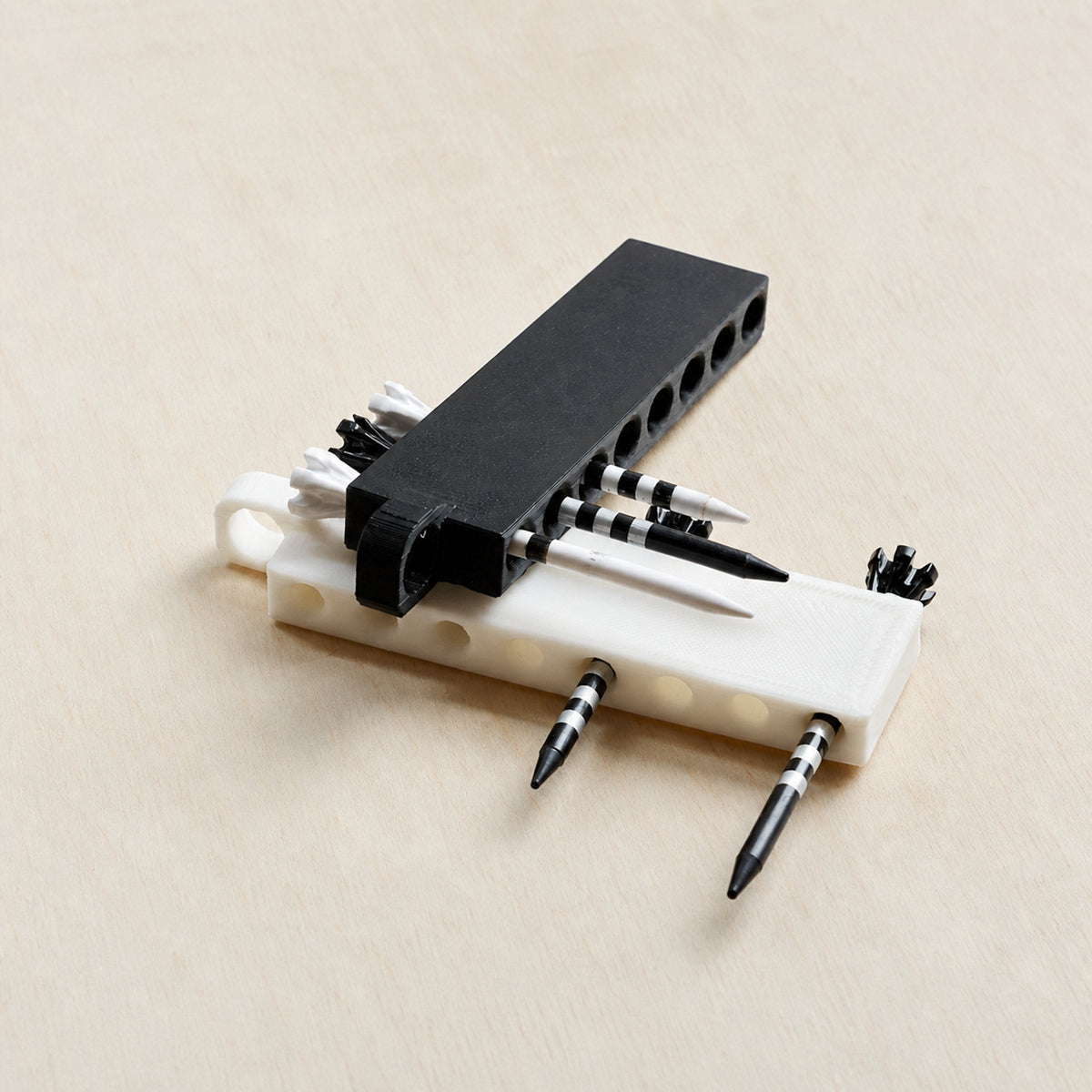 Black and white golf tee holders loaded with tees on a light wood surface