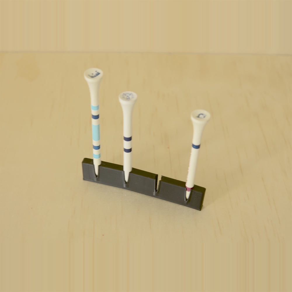 Black wall-mounted golf tee display holding three tees with one position open