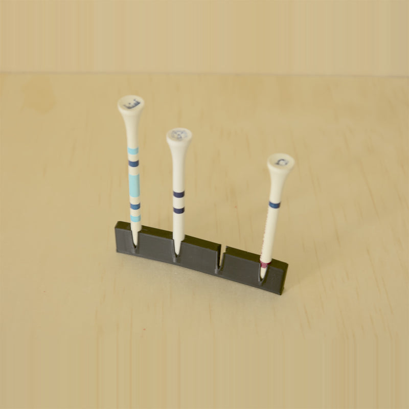 Black wall-mounted golf tee display holding three tees with one position open