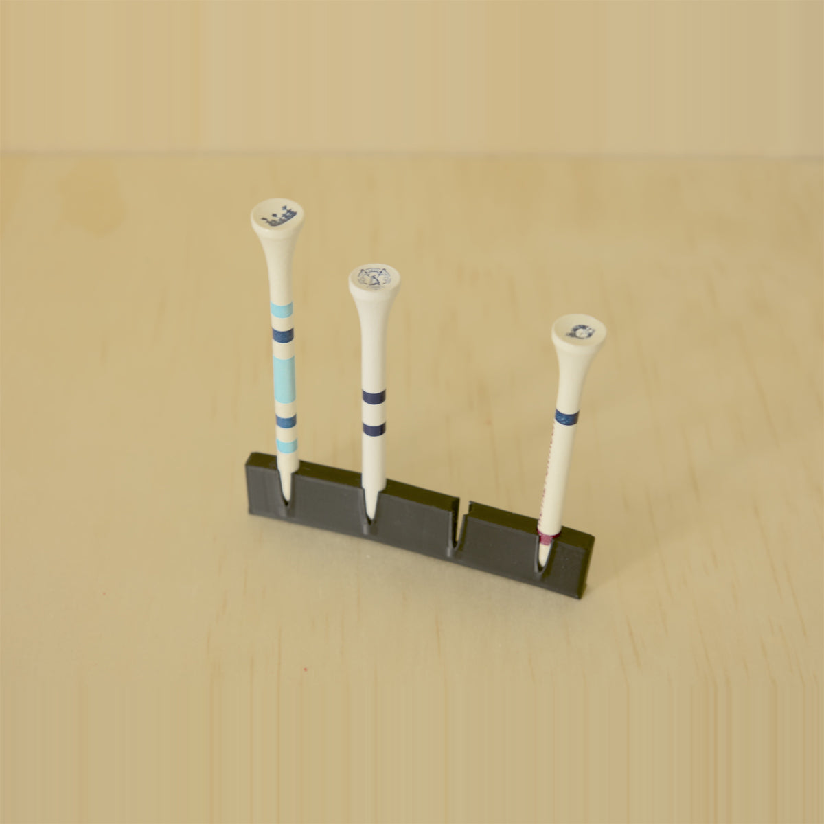 Angled view of a black wall-mounted golf tee display holding three tees