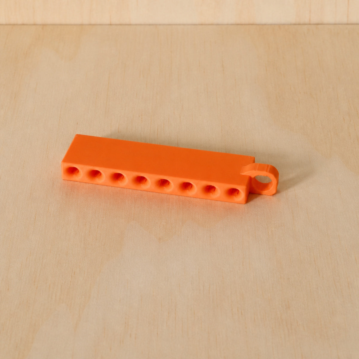 Orange Golf Tee Holder with eight tee openings and hanging loop on pale wood